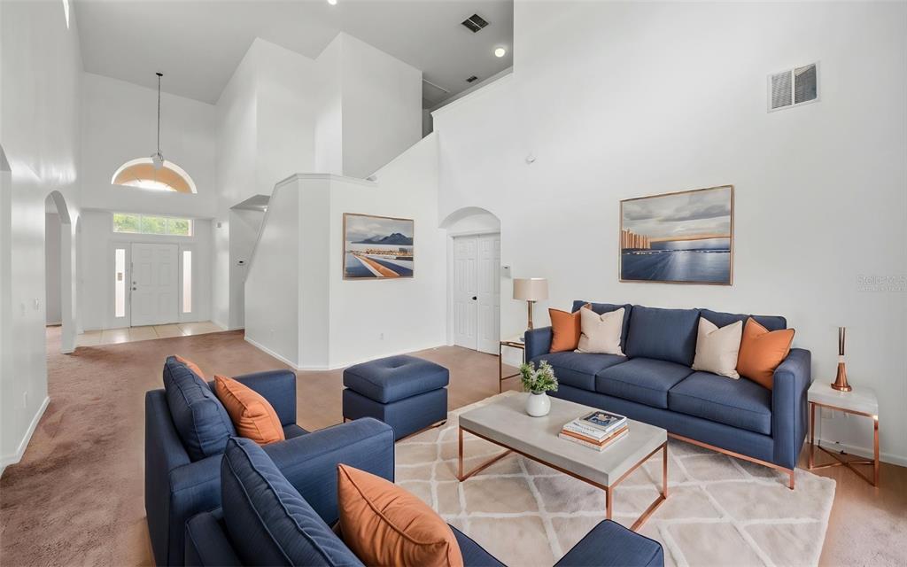 A living room features high ceilings, blue sofas, a coffee table, and a carpeted floor — 2838 SWEETSPIRE CIRCLE, KISSIMMEE, FL