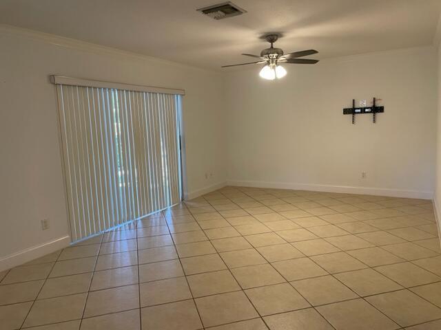 An empty room features light-colored tile flooring, a ceiling fan, and a sliding glass door — 1979 Juno Road, North Palm Beach FL 33408, NORTH PALM BEACH, FL