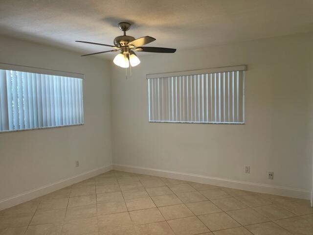 An empty room with white walls, tile flooring, two windows with blinds, and a ceiling fan — 1979 Juno Road, North Palm Beach FL 33408, NORTH PALM BEACH, FL