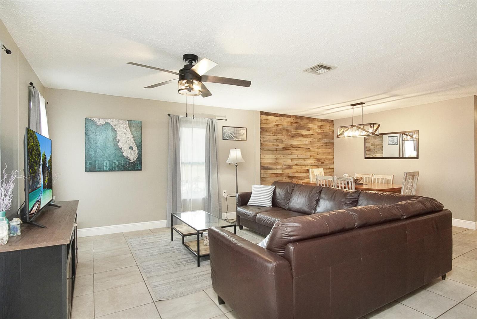 A living room features a brown leather sectional, a wood-paneled accent wall, and tile flooring — 1002 Avenue E E, Fort Pierce FL 34950, FORT PIERCE, FL