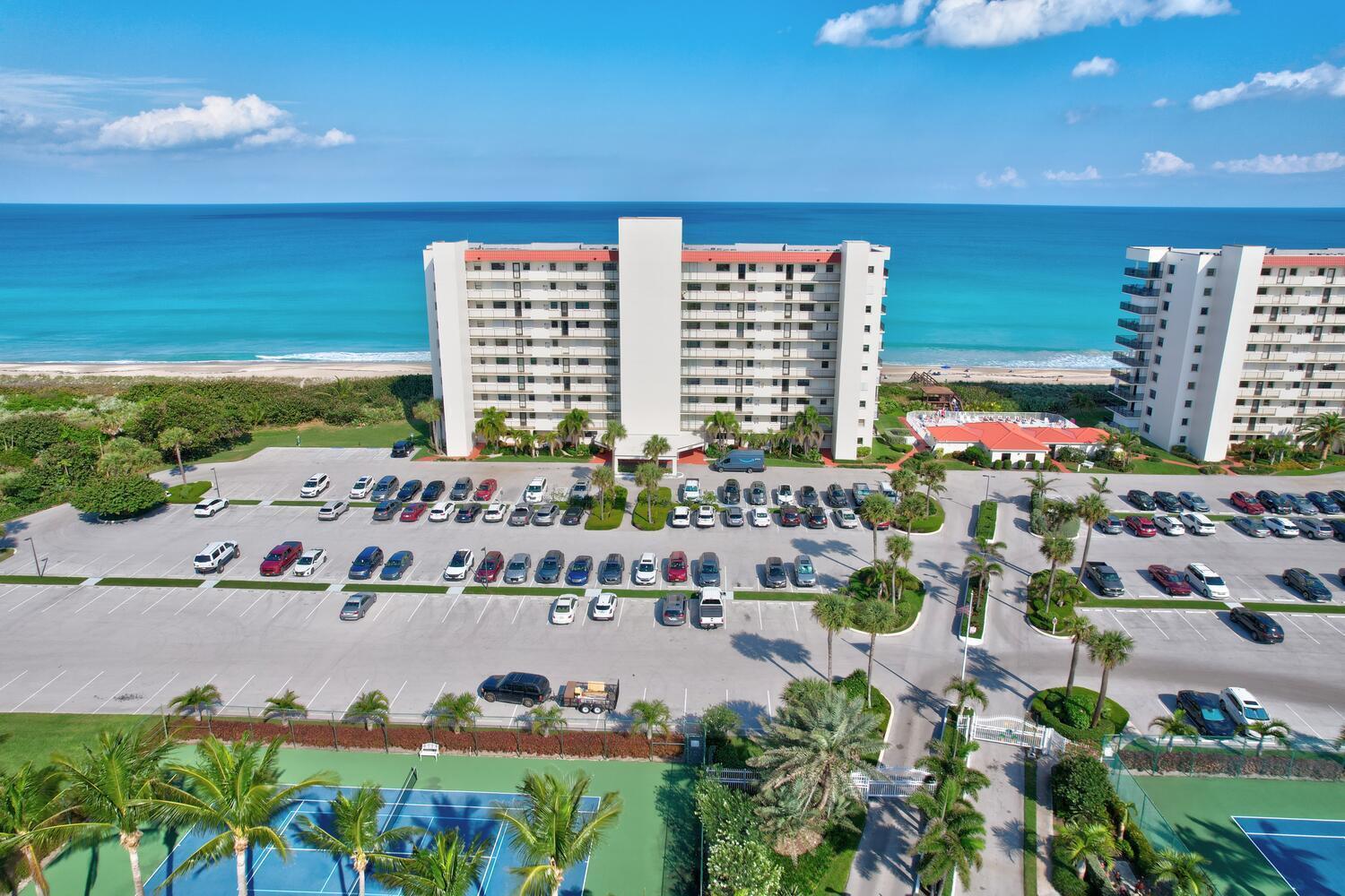 An aerial view shows a large beachfront apartment complex with a parking lot and tennis courts — 9400 S Ocean Drive # 807, Jensen Beach FL 34957, JENSEN BEACH, FL