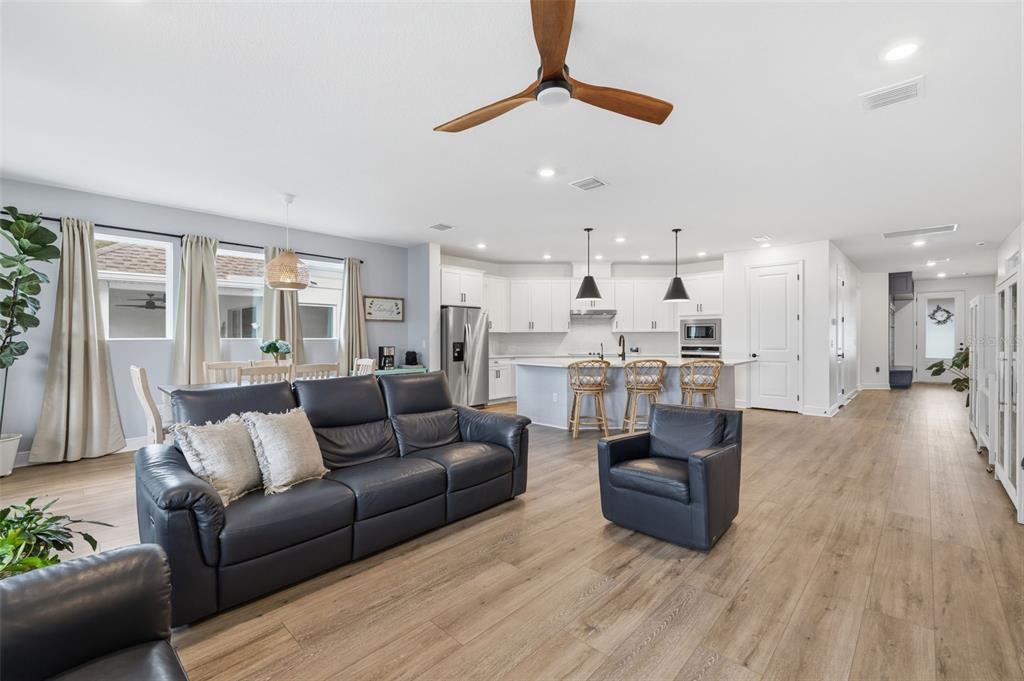 An open-concept living room and kitchen featuring light wood floors, white cabinetry, and leather furniture — 1455 GOPHER LOOP, TARPON SPRINGS, FL