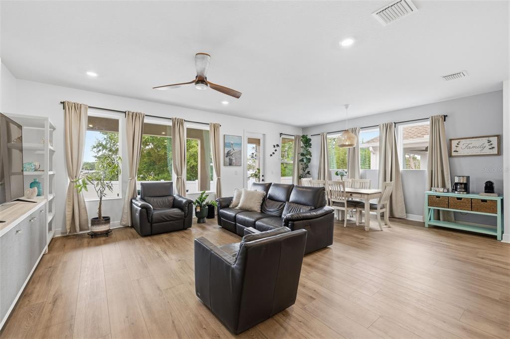 A living room and dining area feature light wood flooring, leather furniture, and large windows — 1455 GOPHER LOOP, TARPON SPRINGS, FL