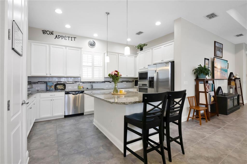 A kitchen features white cabinetry, granite countertops, a center island, and stainless steel appliances — 9189 MERRIFIELD STREET, ORLANDO, FL