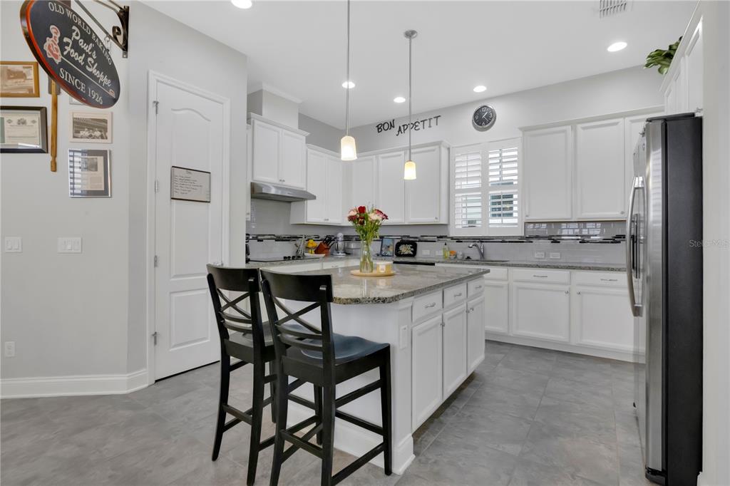 A kitchen features white cabinets, a granite-topped island with two stools, and gray tile flooring — 9189 MERRIFIELD STREET, ORLANDO, FL