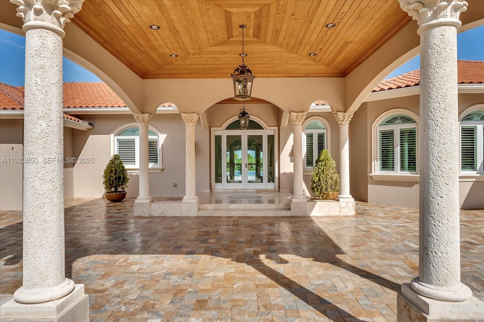 A covered stone patio features classical columns, a wood-paneled ceiling, and a glass-paned entryway — 18611 SW 122nd St, Miami FL 33196, MIAMI, FL