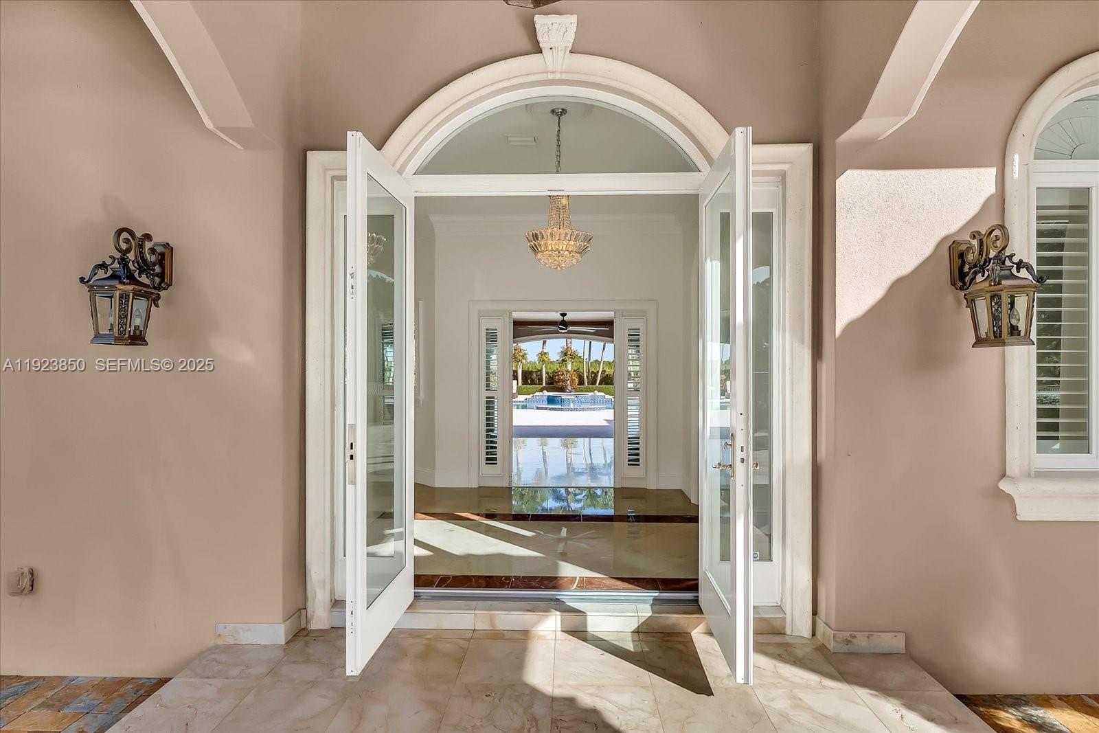 An open double door reveals a foyer with a crystal chandelier and a backyard pool — 18611 SW 122nd St, Miami FL 33196, MIAMI, FL