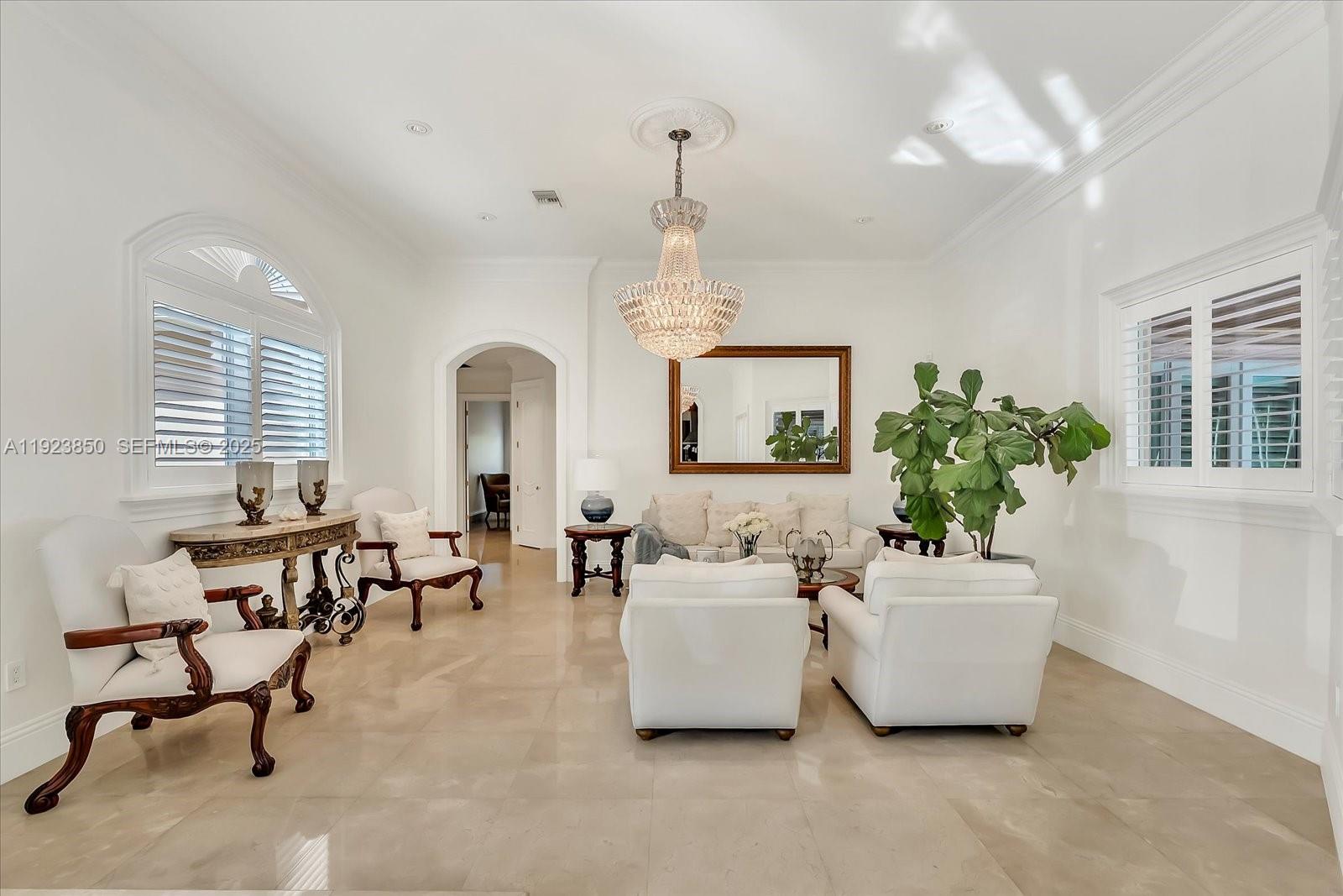A bright living room features white furniture, a crystal chandelier, and large arched windows — 18611 SW 122nd St, Miami FL 33196, MIAMI, FL