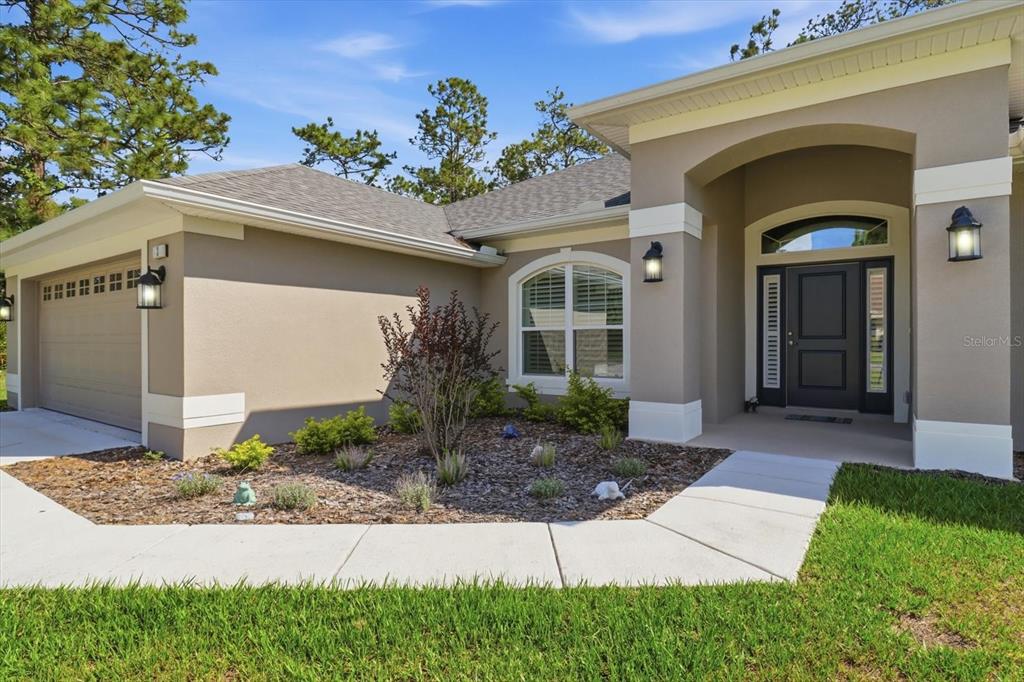 The exterior of a single-story house features a tan stucco facade, a garage, and landscaping — 3 STOKESIA COURT, HOMOSASSA, FL