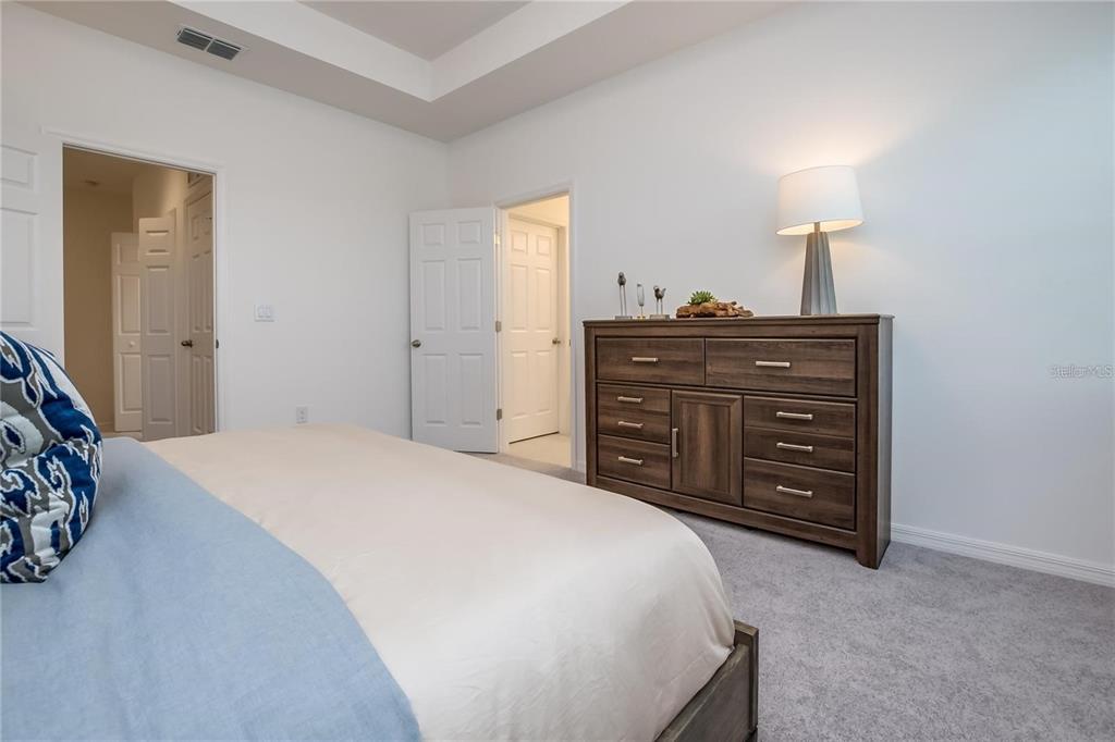 A bedroom features a bed, a wooden dresser with a lamp, and two open doorways — 1200 WYCLIFFE WAY, ST CLOUD, FL