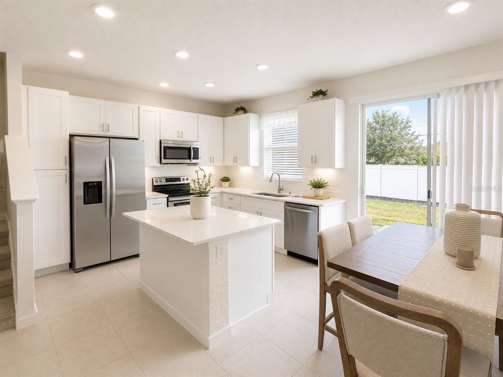A bright kitchen features white cabinets, stainless steel appliances, a central island, and dining area — 1200 WYCLIFFE WAY, ST CLOUD, FL