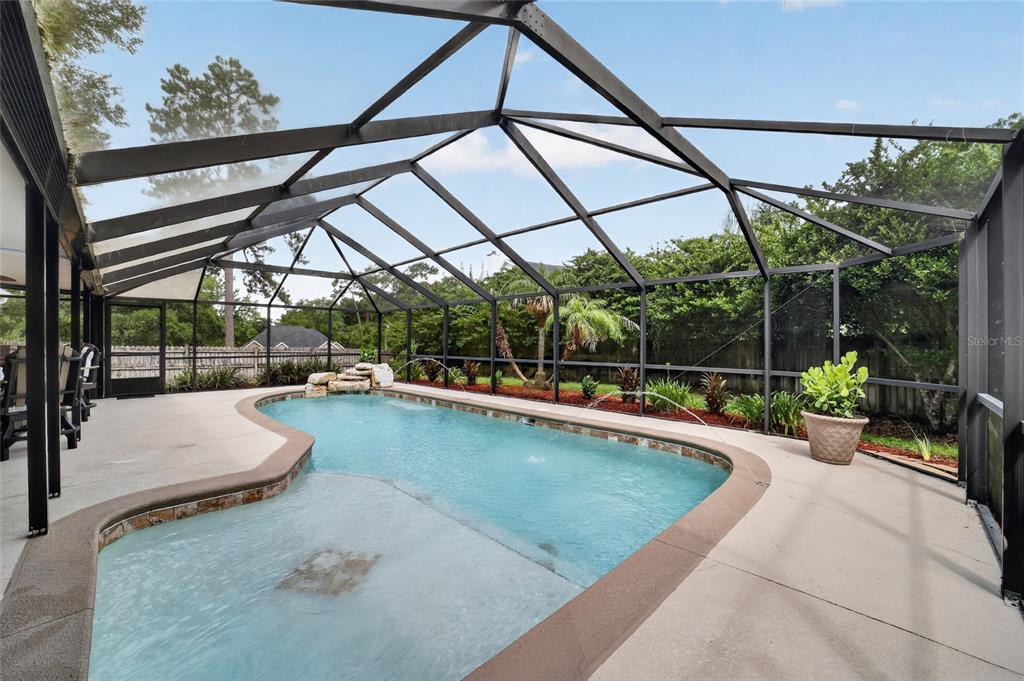 A swimming pool with a rock waterfall feature is enclosed by a screened-in patio — 4823 SE 14TH STREET, OCALA, FL