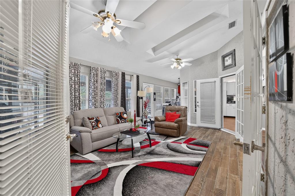 A living room with a vaulted ceiling, ceiling fans, tile floors, and a patterned area rug — 4823 SE 14TH STREET, OCALA, FL