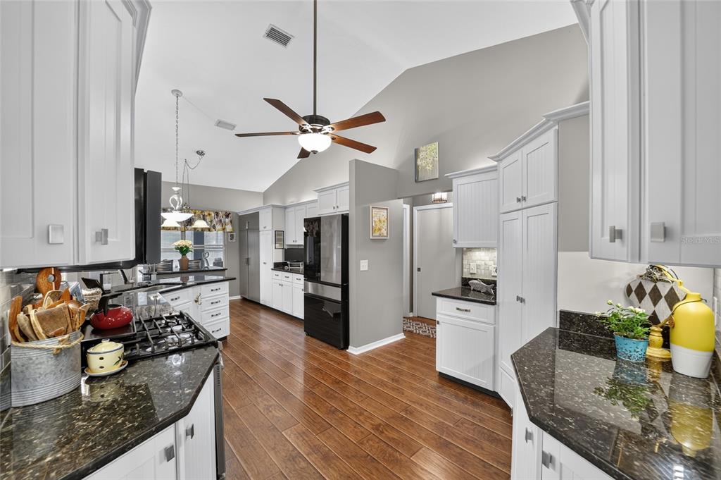 A kitchen with white cabinets, dark granite countertops, stainless steel appliances, and wood-look flooring — 4823 SE 14TH STREET, OCALA, FL