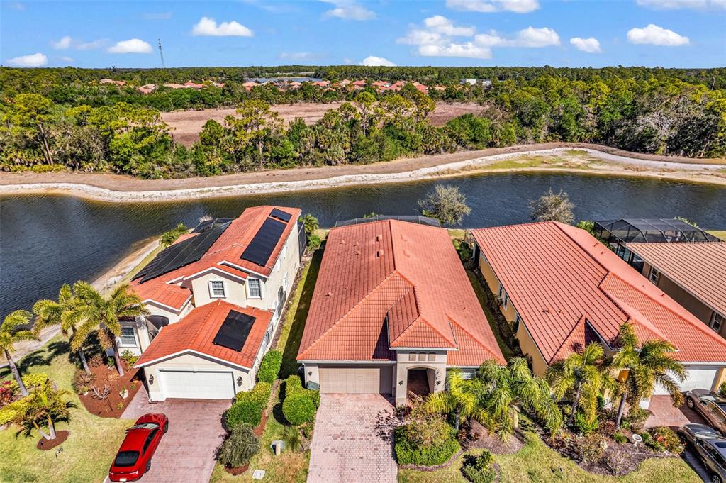 An aerial view shows three suburban houses with red tile roofs situated along a canal — 11542 BLACKFIN STREET, VENICE, FL