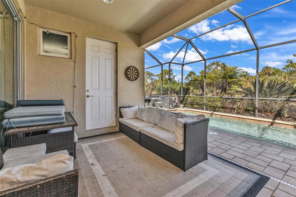 A covered patio features a sofa, a dartboard, and a screened-in pool area — 11542 BLACKFIN STREET, VENICE, FL