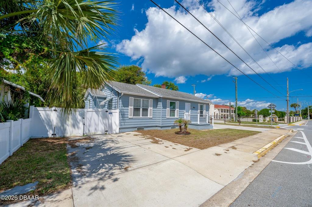A light blue single-story house with a white fence and concrete driveway under a blue sky — 243 N PENINSULA DRIVE, DAYTONA BEACH, FL