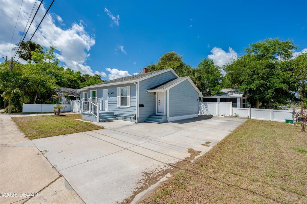A light blue, single-story house features a concrete driveway and a white vinyl fence — 243 N PENINSULA DRIVE, DAYTONA BEACH, FL