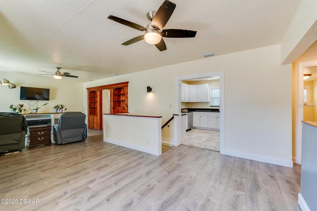 A living room with wood-look flooring leads to a kitchen through an open doorway — 243 N PENINSULA DRIVE, DAYTONA BEACH, FL
