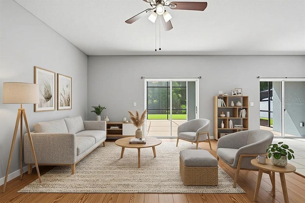 This digitally staged living room features light gray walls, wood flooring, and a sliding glass door — 18318 HOLLAND HOUSE LOOP, LAND O LAKES, FL
