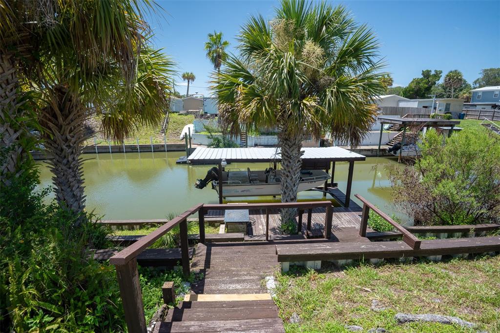 A wooden staircase leads down to a boat dock on a canal with palm trees — 110 CHARLES STREET, EDGEWATER, FL