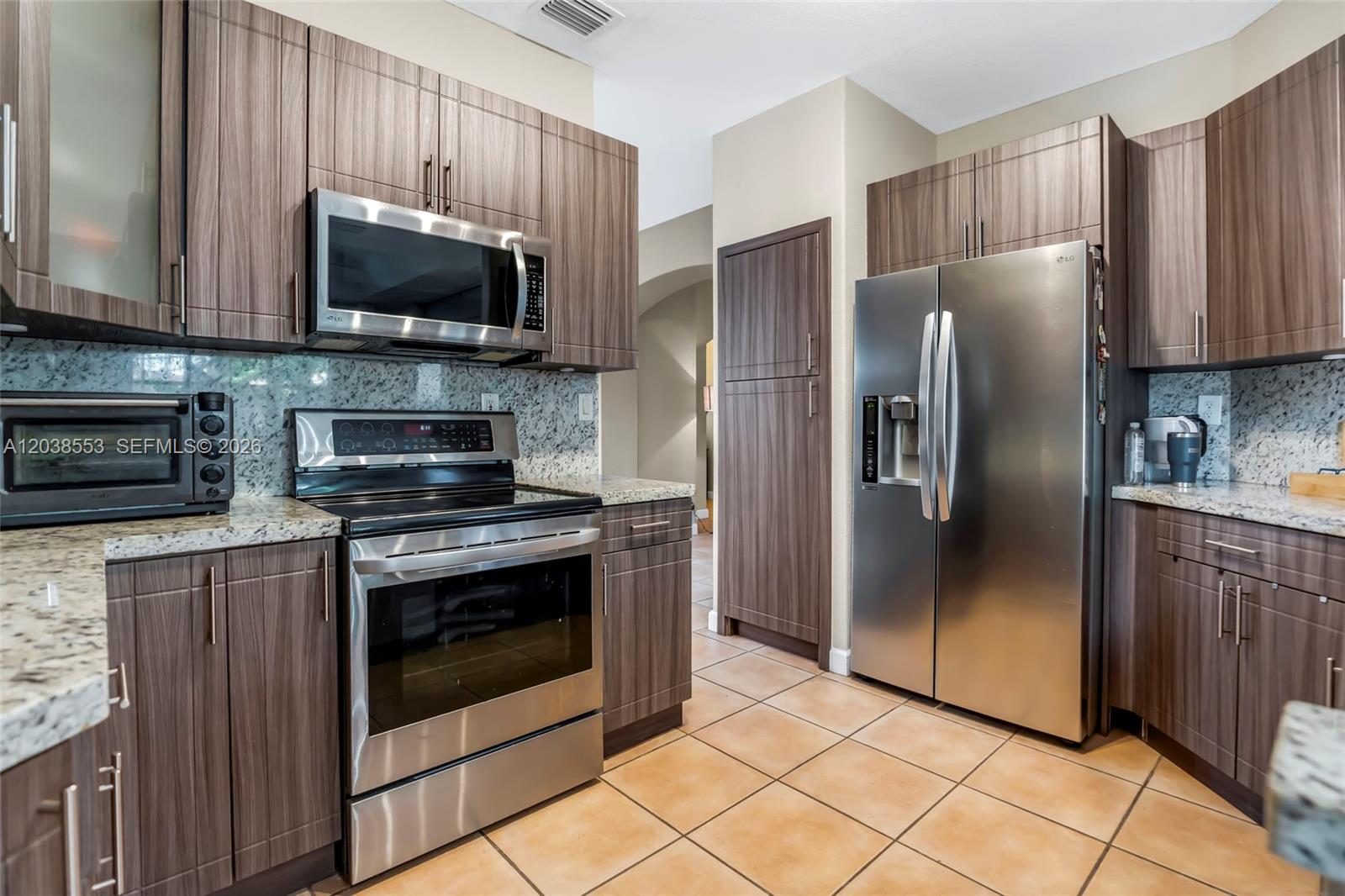 A kitchen features wood-grain cabinets, stainless steel appliances, and granite countertops over tiled flooring — 16728 SW 36th St, Miramar FL 33027, MIRAMAR, FL