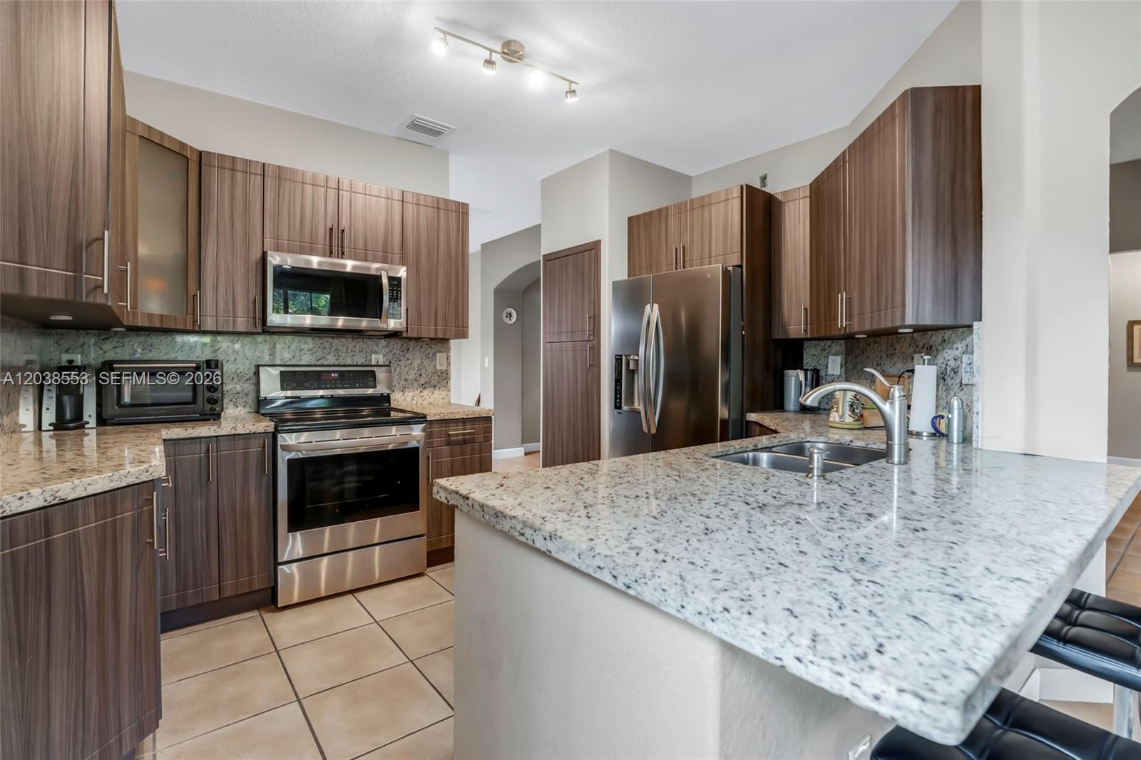 A kitchen features dark wood cabinets, granite countertops, and stainless steel appliances — 16728 SW 36th St, Miramar FL 33027, MIRAMAR, FL