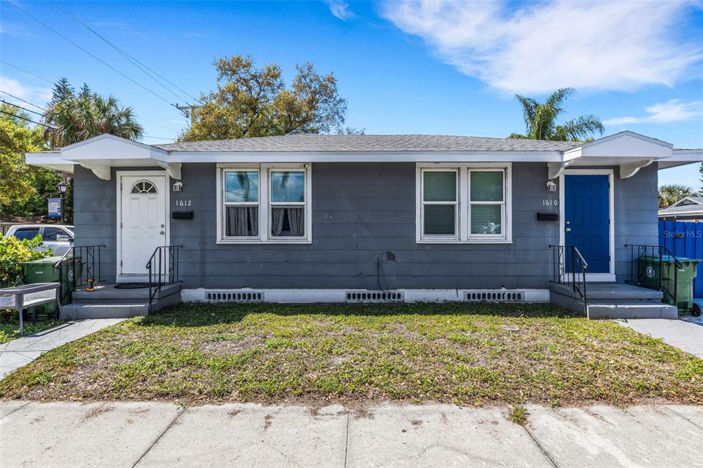 A single-story duplex with gray siding, two front doors, and a small front yard — 1608, 1610, 1612 11TH STREET W, BRADENTON, FL