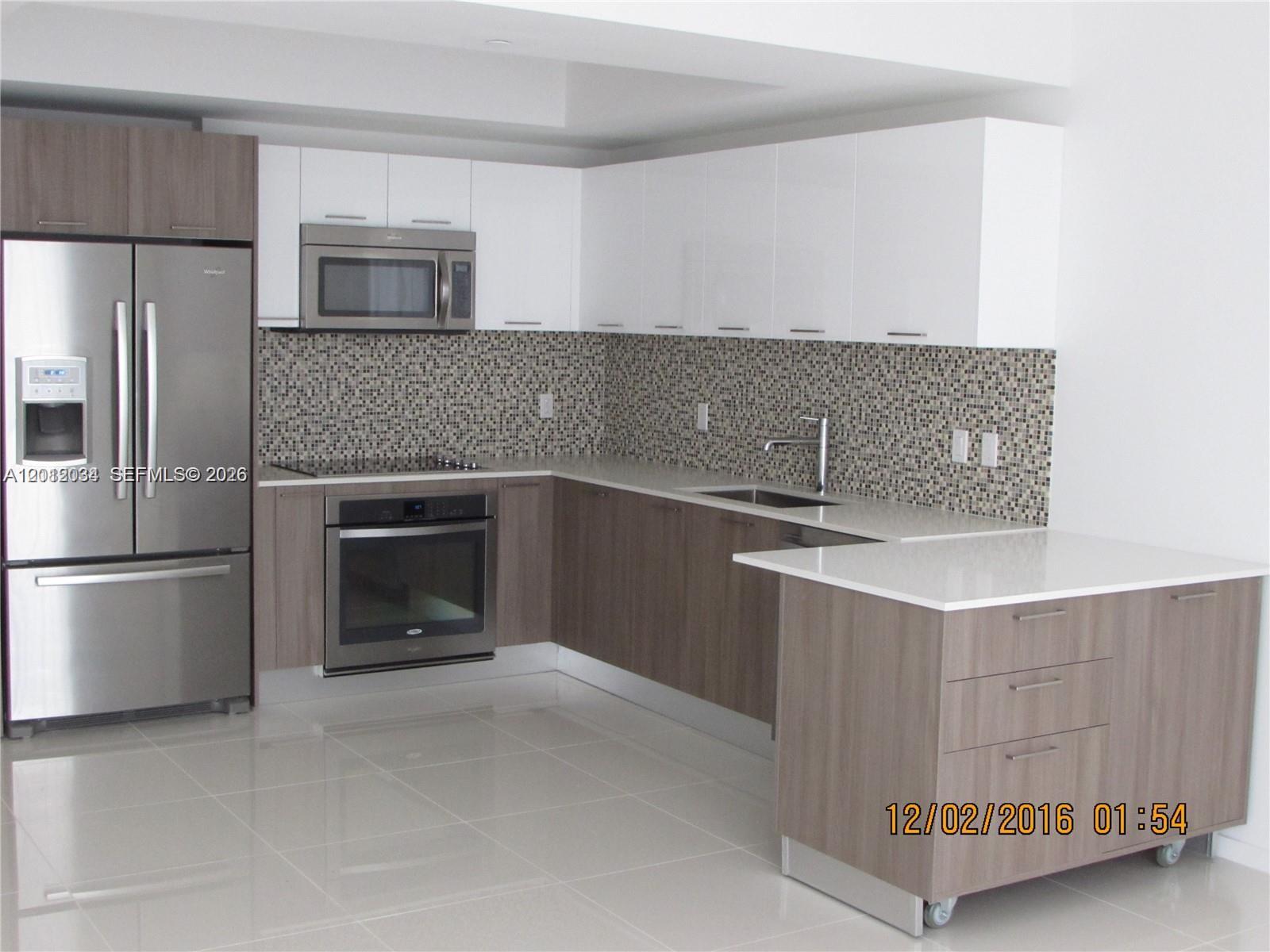 A modern kitchen features two-tone cabinets, stainless steel appliances, a mosaic backsplash, and a rolling island — 5300 Paseo Blvd # 405, Doral FL 33166, DORAL, FL