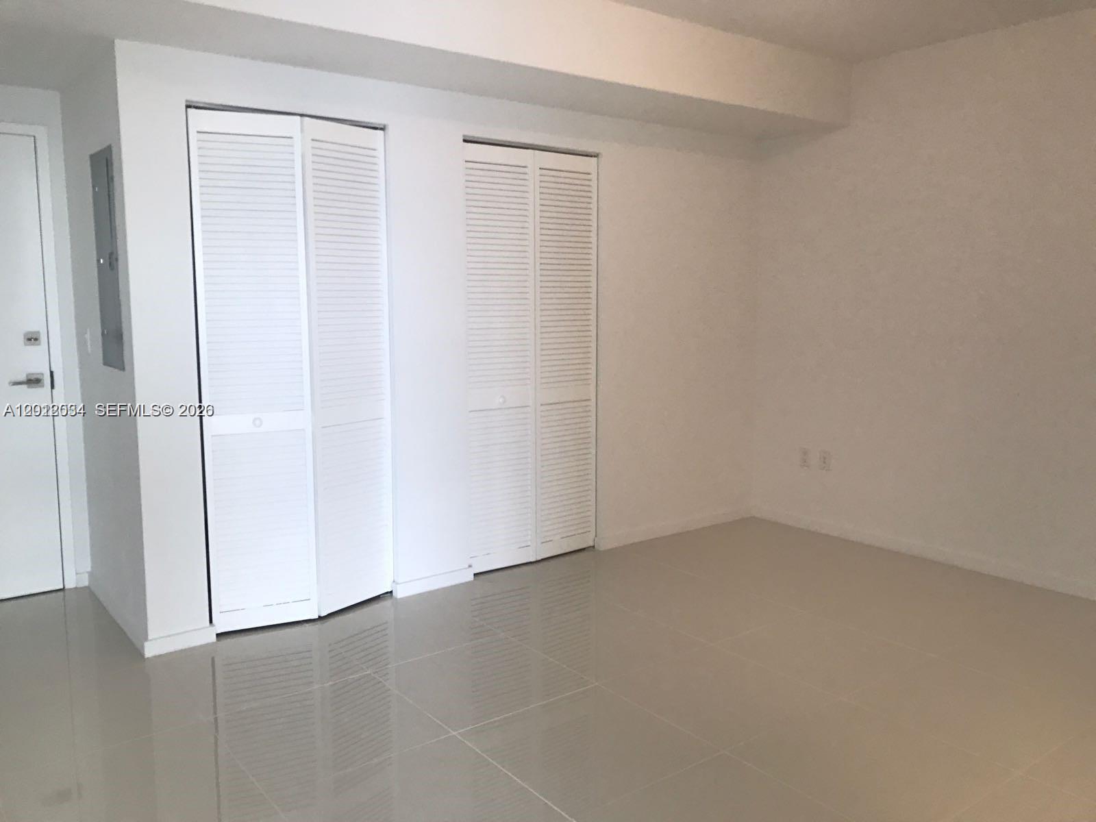 An empty room features white walls, light-colored tile flooring, and two sets of louvered closet doors — 5300 Paseo Blvd # 405, Doral FL 33166, DORAL, FL