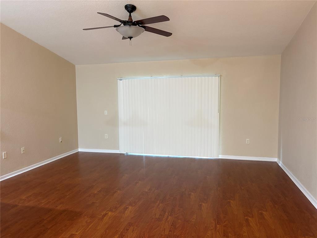 An empty room features wood-look flooring, beige walls, a ceiling fan, and vertical window blinds — 9832 SW 196TH AVENUE ROAD, DUNNELLON, FL