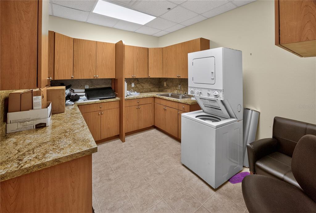 A kitchen or breakroom features wood cabinets, granite countertops, a sink, and a stacked washer-dryer — 733 COUNTY ROAD 466, LADY LAKE, FL