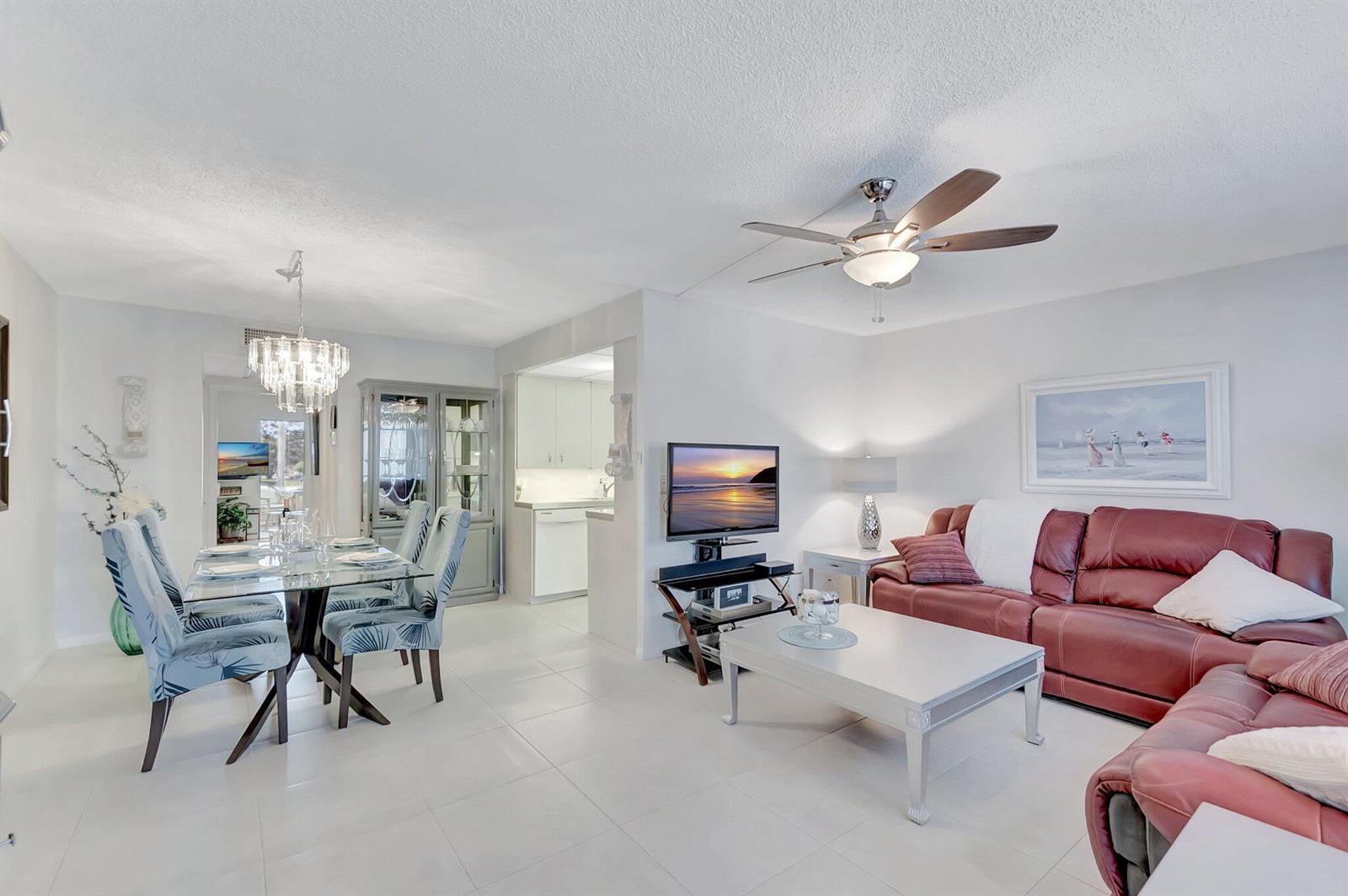 An open-concept living and dining room with white tile floors, a red sofa, and chandelier — 2051 Cambridge C, Deerfield Beach FL 33442, DEERFIELD BEACH, FL