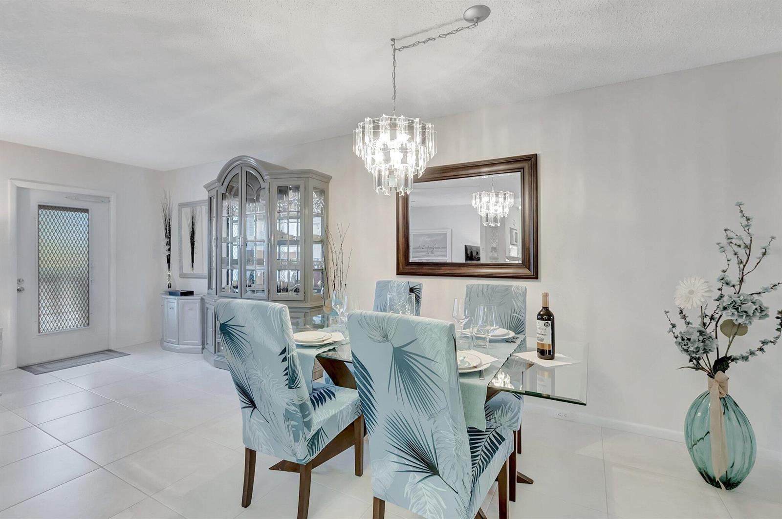 A dining room features a glass table, palm-print chairs, a crystal chandelier, and a china cabinet — 2051 Cambridge C, Deerfield Beach FL 33442, DEERFIELD BEACH, FL