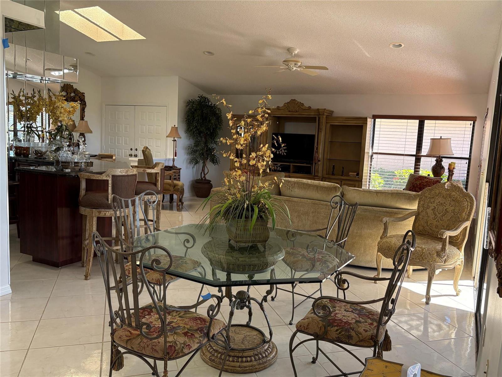 An open-concept living and dining area features tile flooring, a glass-topped table, and bar seating — 7744 Dundee Lane, Delray Beach FL 33446, DELRAY BEACH, FL
