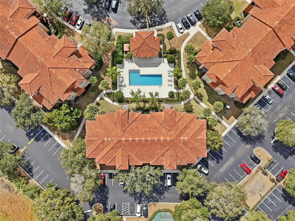 An aerial view shows apartment buildings with terracotta roofs surrounding a central swimming pool area — 5518 METROWEST BOULEVARD UNIT 11-104, ORLANDO, FL