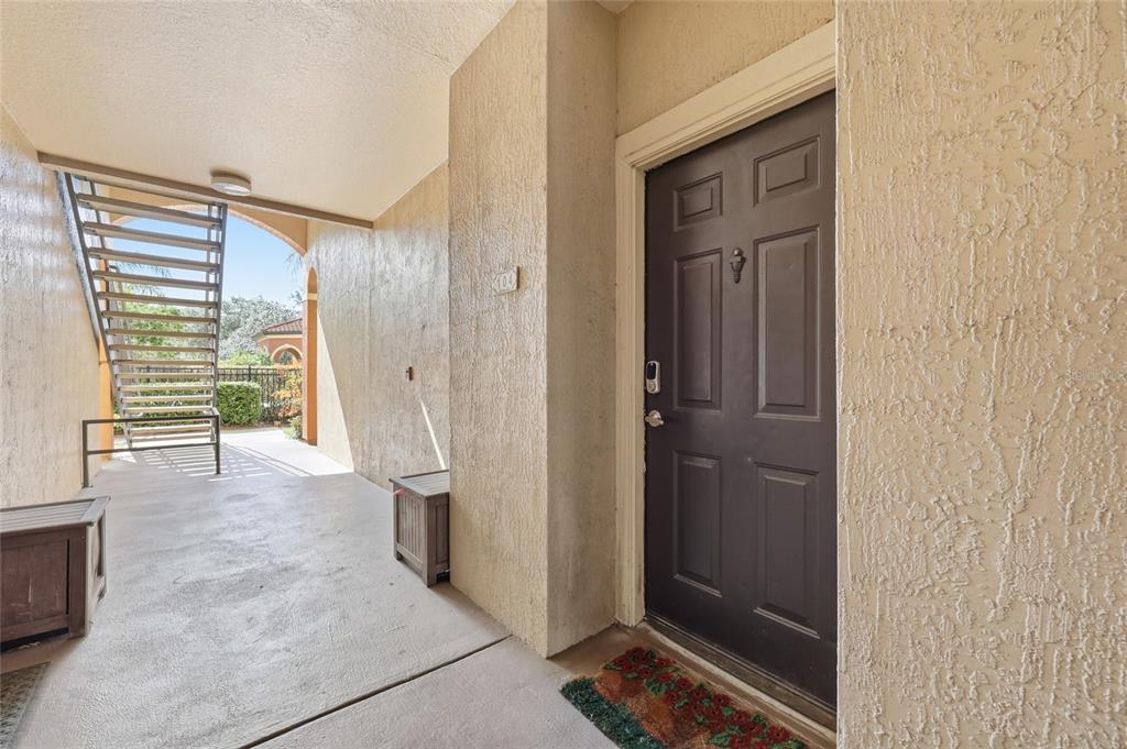 A dark brown front door is situated on a covered concrete walkway with metal stairs — 5518 METROWEST BOULEVARD UNIT 11-104, ORLANDO, FL