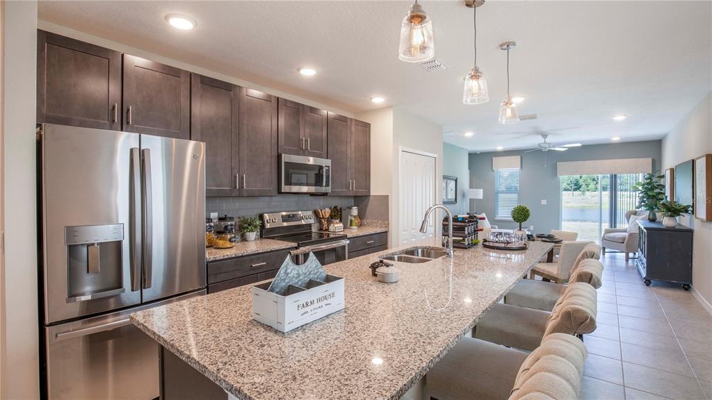 A kitchen features dark wood cabinets, granite countertops, a large island, and stainless steel appliances — 3928 BLUETHREAD WAY, POINCIANA, FL