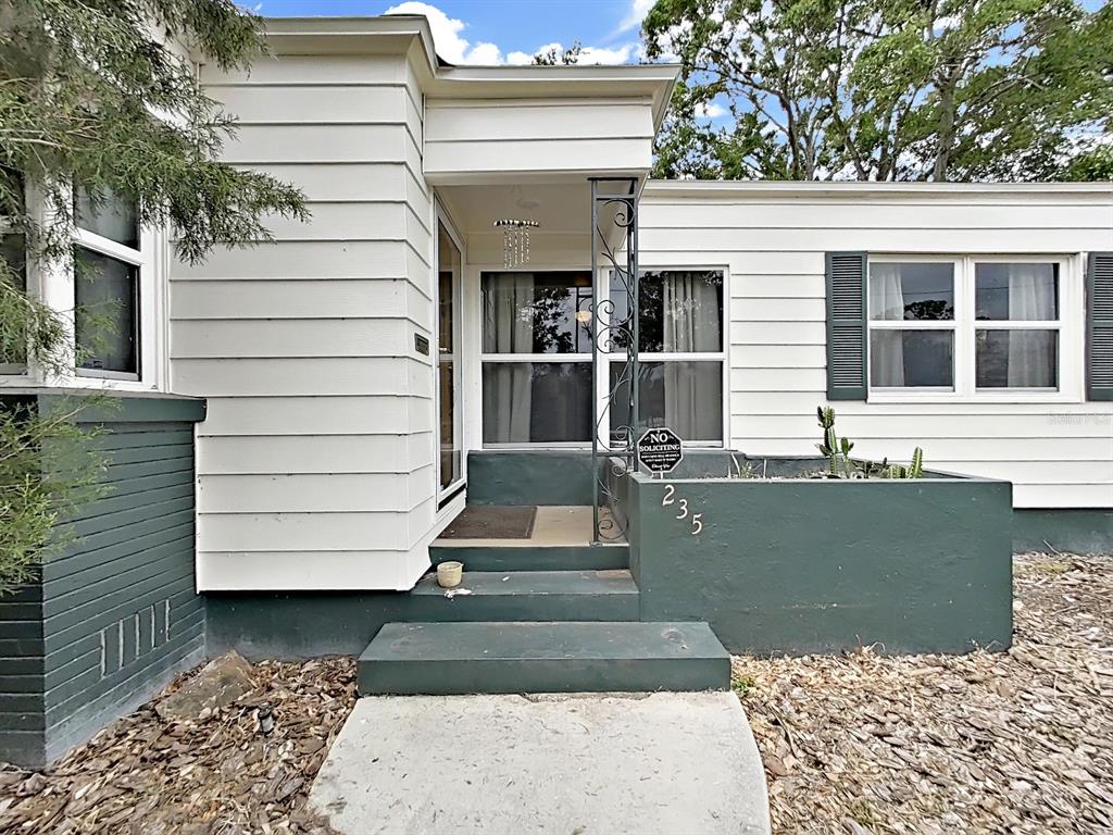 The exterior of a house features white siding, a green concrete porch, and a small planter — 235 38TH STREET S, ST PETERSBURG, FL
