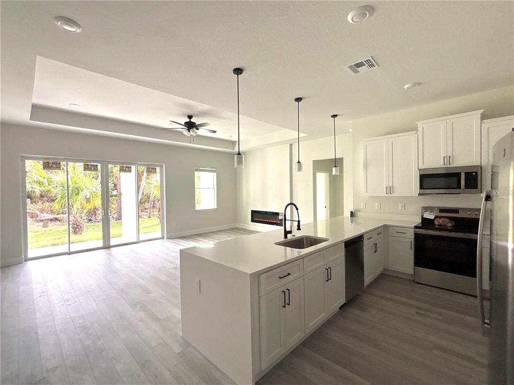 A modern kitchen with white cabinets, quartz countertops, and an island overlooks a living area — 3068 VELVET LANE, NORTH PORT, FL
