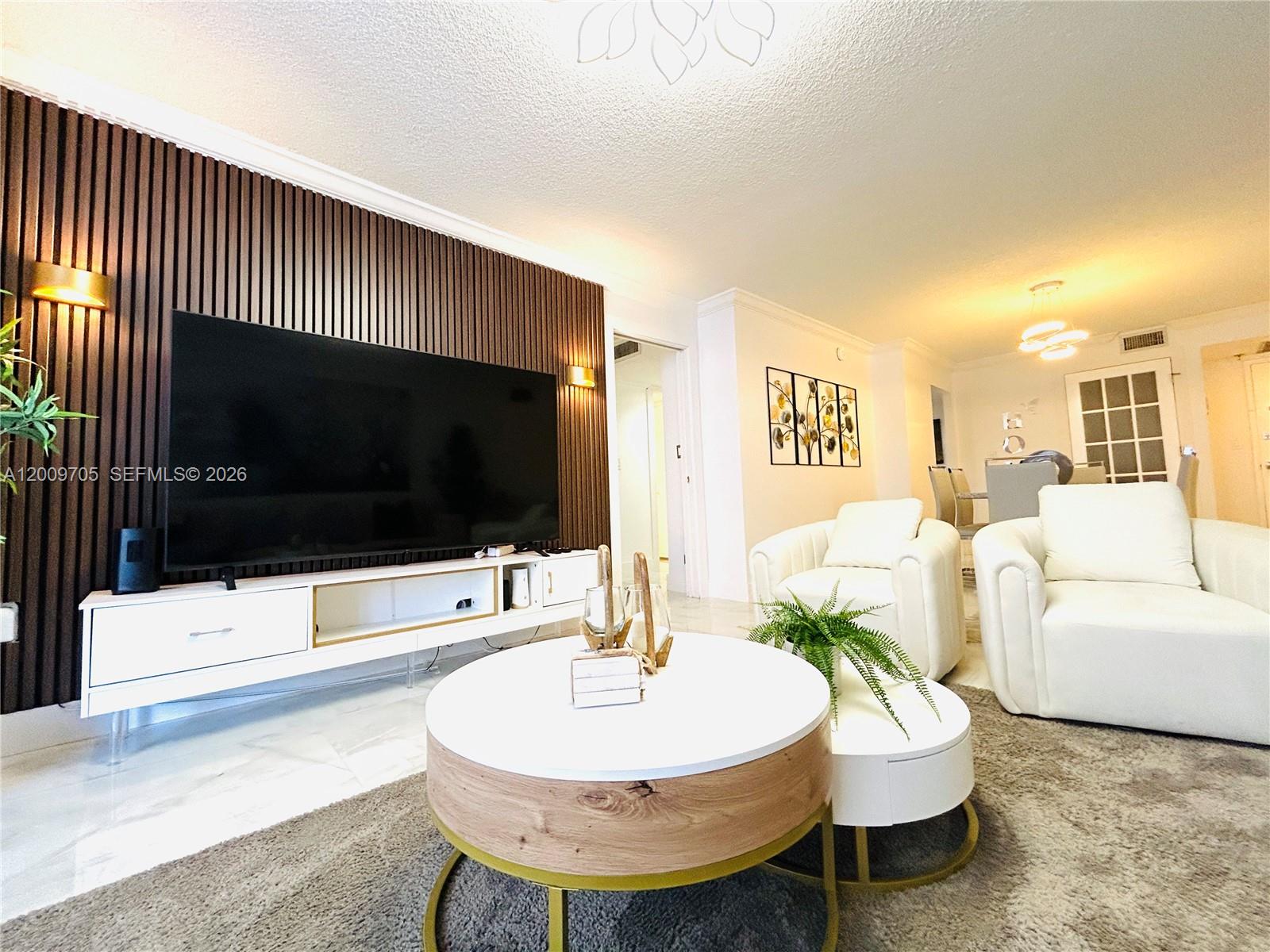A living room features a slatted wood accent wall, a large television, and white furniture — 6039 Collins Ave # 1507, Miami Beach FL 33140, MIAMI BEACH, FL