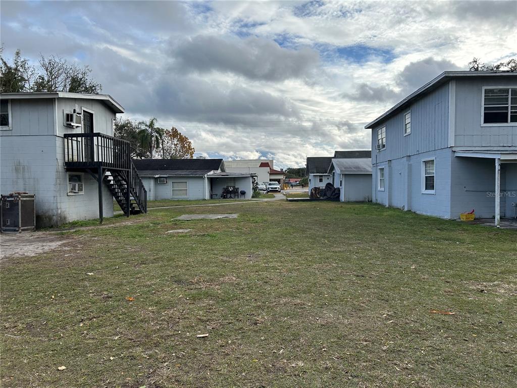 A grassy yard sits between two light blue multi-story buildings under a cloudy sky — 6015 FOREST CITY ROAD, ORLANDO, FL