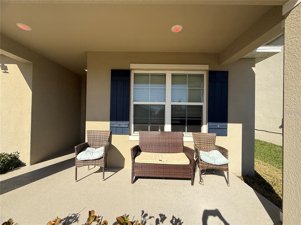 A covered concrete porch features a wicker loveseat and two matching chairs with cushions — 5696 GALLOPING DRIVE, APOPKA, FL