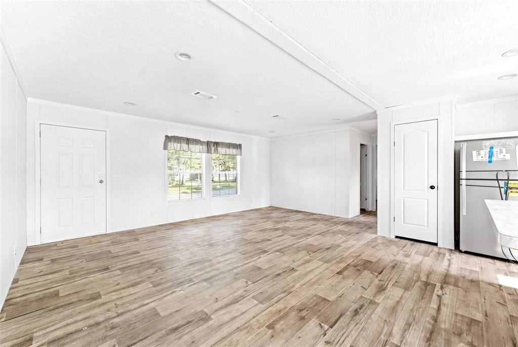 An open-concept living area features white walls, wood-look flooring, and a stainless steel refrigerator — 5207 ORANGE AVENUE, PORT ORANGE, FL