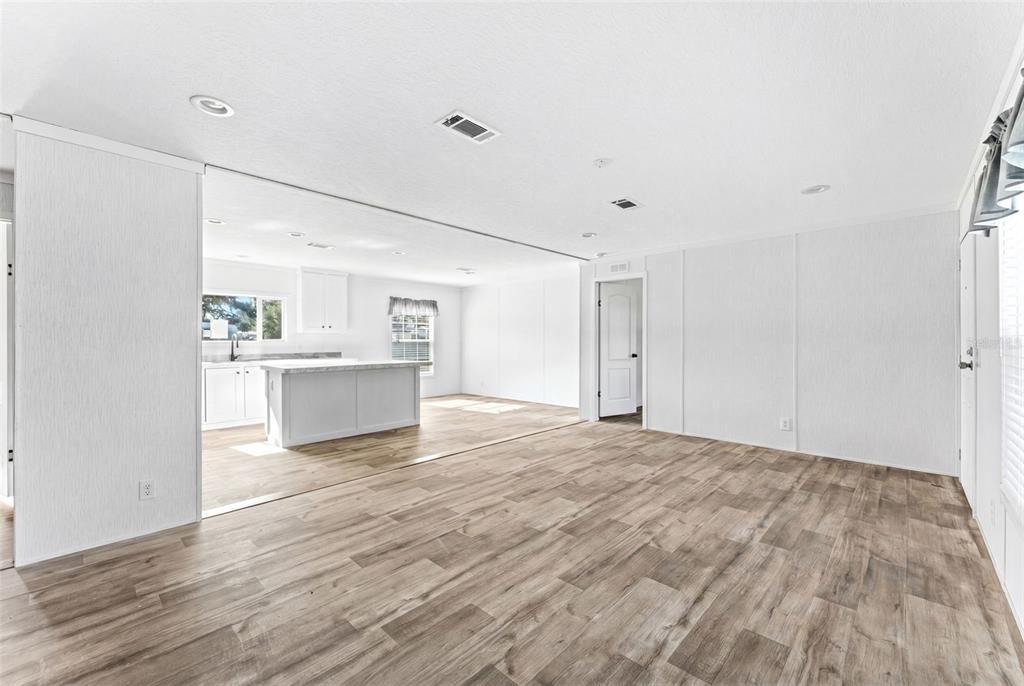 A bright, open-concept living area with wood-look flooring flows into a kitchen with white cabinetry — 5207 ORANGE AVENUE, PORT ORANGE, FL