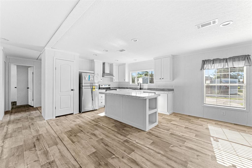 A bright kitchen features white cabinetry, a central island, and wood-look flooring — 5207 ORANGE AVENUE, PORT ORANGE, FL