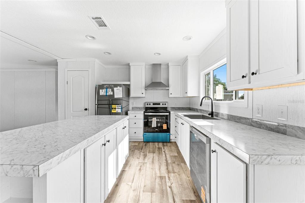 A kitchen features white cabinets, marble-patterned countertops, stainless steel appliances, and wood-look flooring — 5207 ORANGE AVENUE, PORT ORANGE, FL