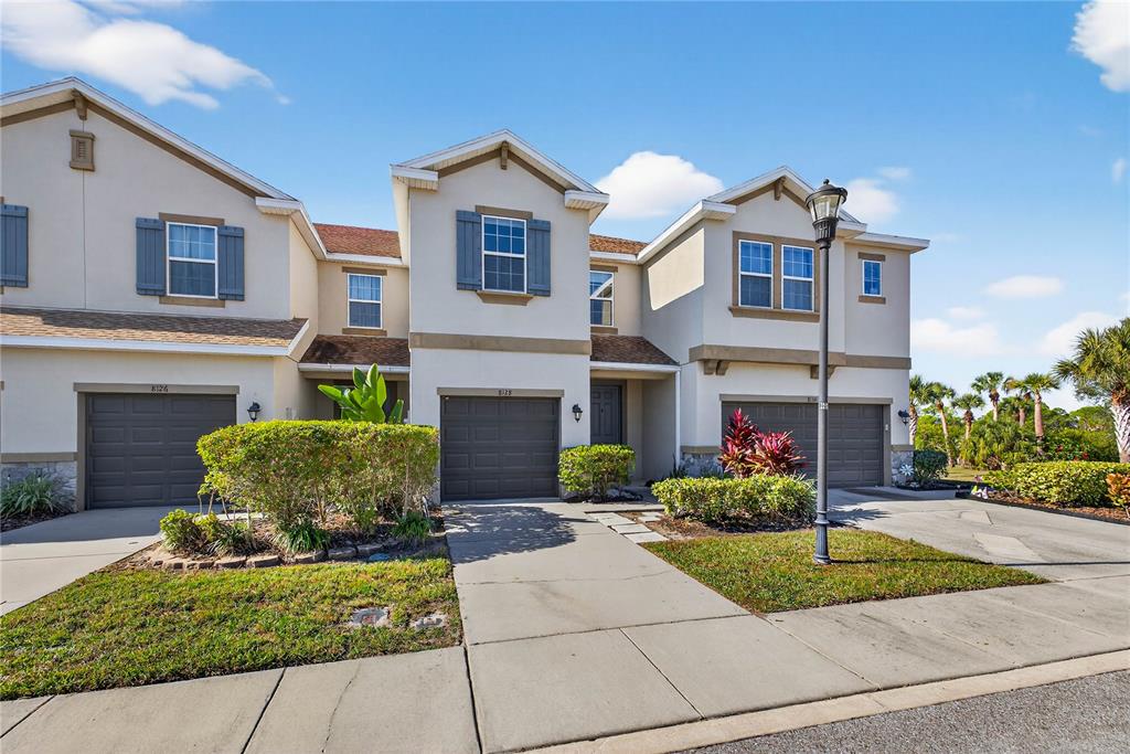 A row of three attached townhouses features beige stucco exteriors, brown garage doors, and landscaped lawns — 8128 MUDDY PINES PLACE, TAMPA, FL