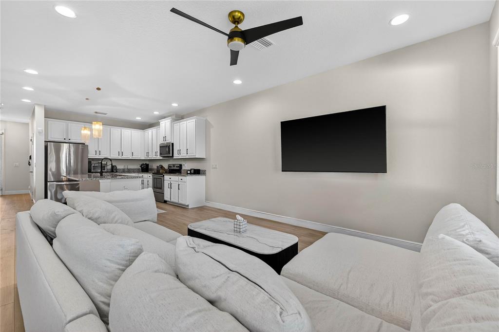 A modern living room with a large sectional sofa faces a wall-mounted television — 8128 MUDDY PINES PLACE, TAMPA, FL