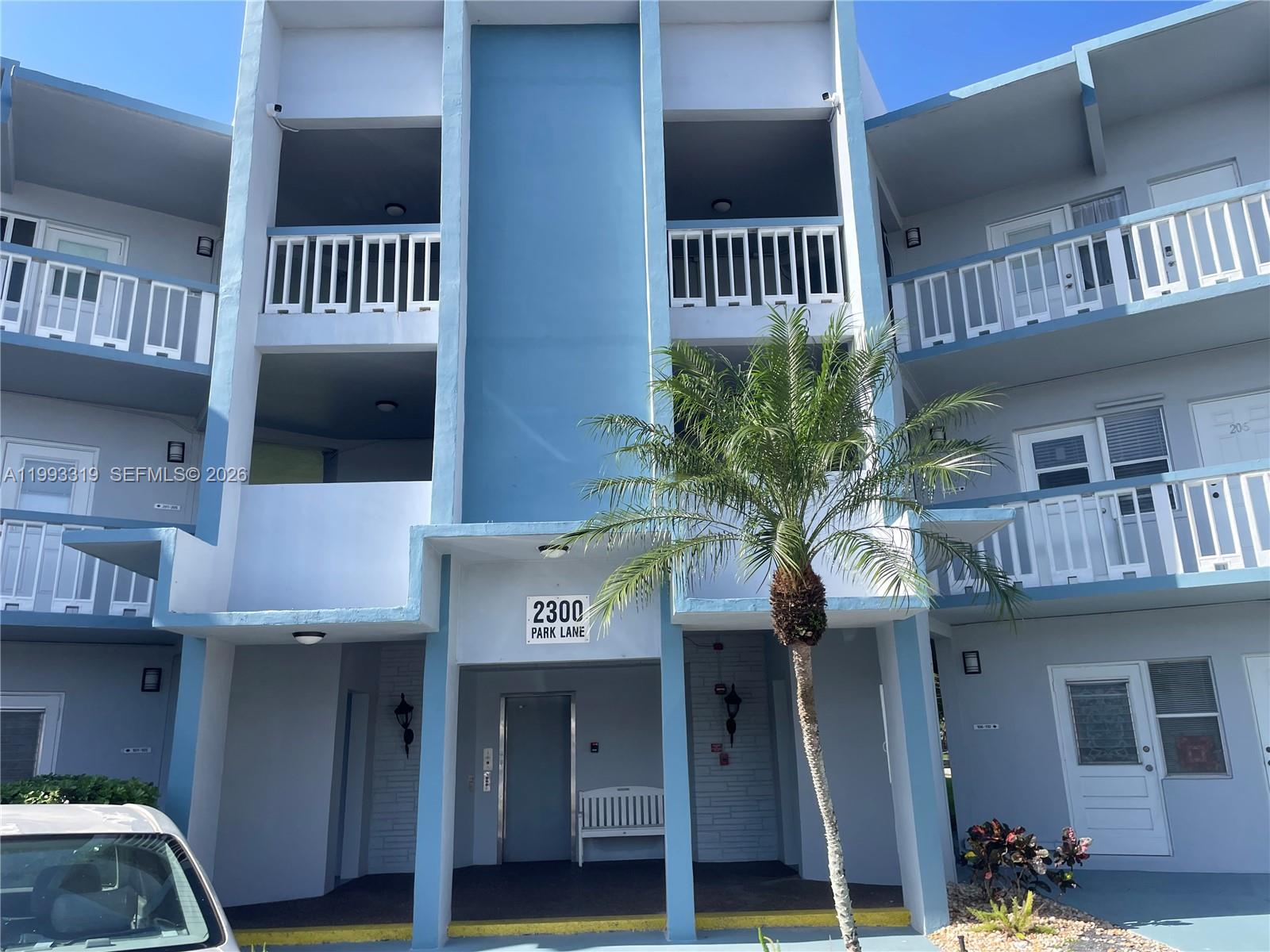 A three-story blue apartment building features white railings, a palm tree, and a central entrance — 2300 Park Ln # 208, Hollywood FL 33021, HOLLYWOOD, FL
